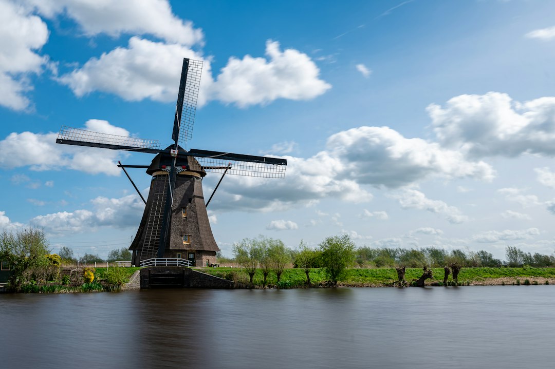 Nederlandse windmolen aan een rivier onder een blauwe lucht met wolken